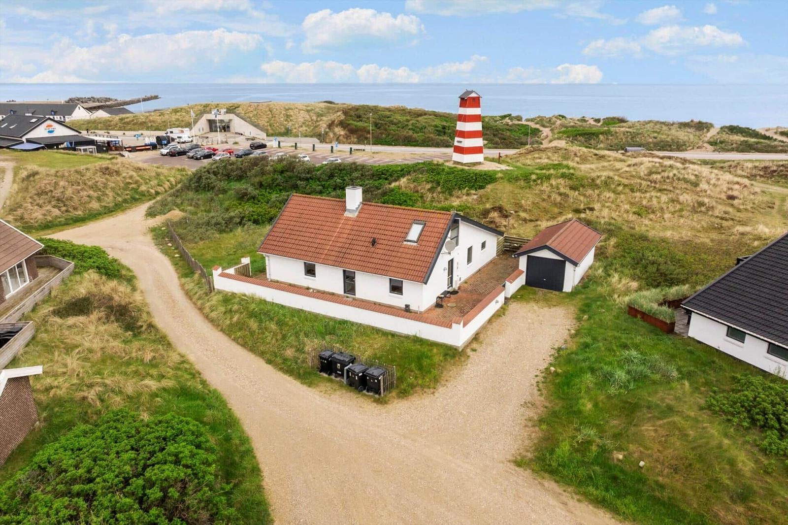 Wohnhaus mit rotem Dach und rotem Schuppen, nahe Leuchtturm und Strand.