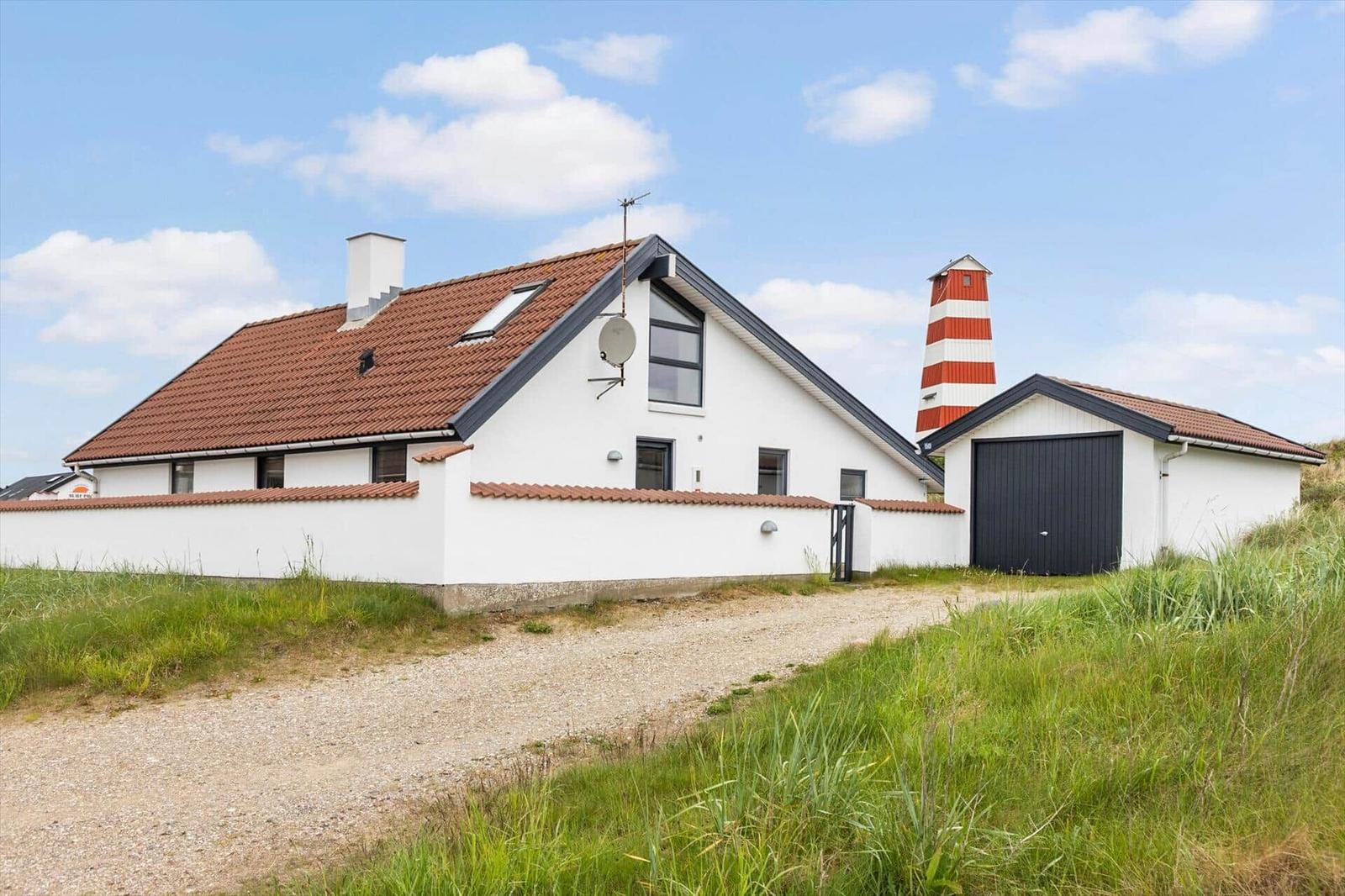 Wohnhaus mit rotem Dach und weißer Fassade, daneben steht ein roter Leuchtturm.