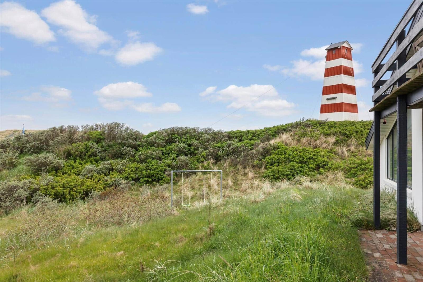 Rotes und weißes Leuchtturmhaus mit Grünfläche und Schaukel im Vordergrund.