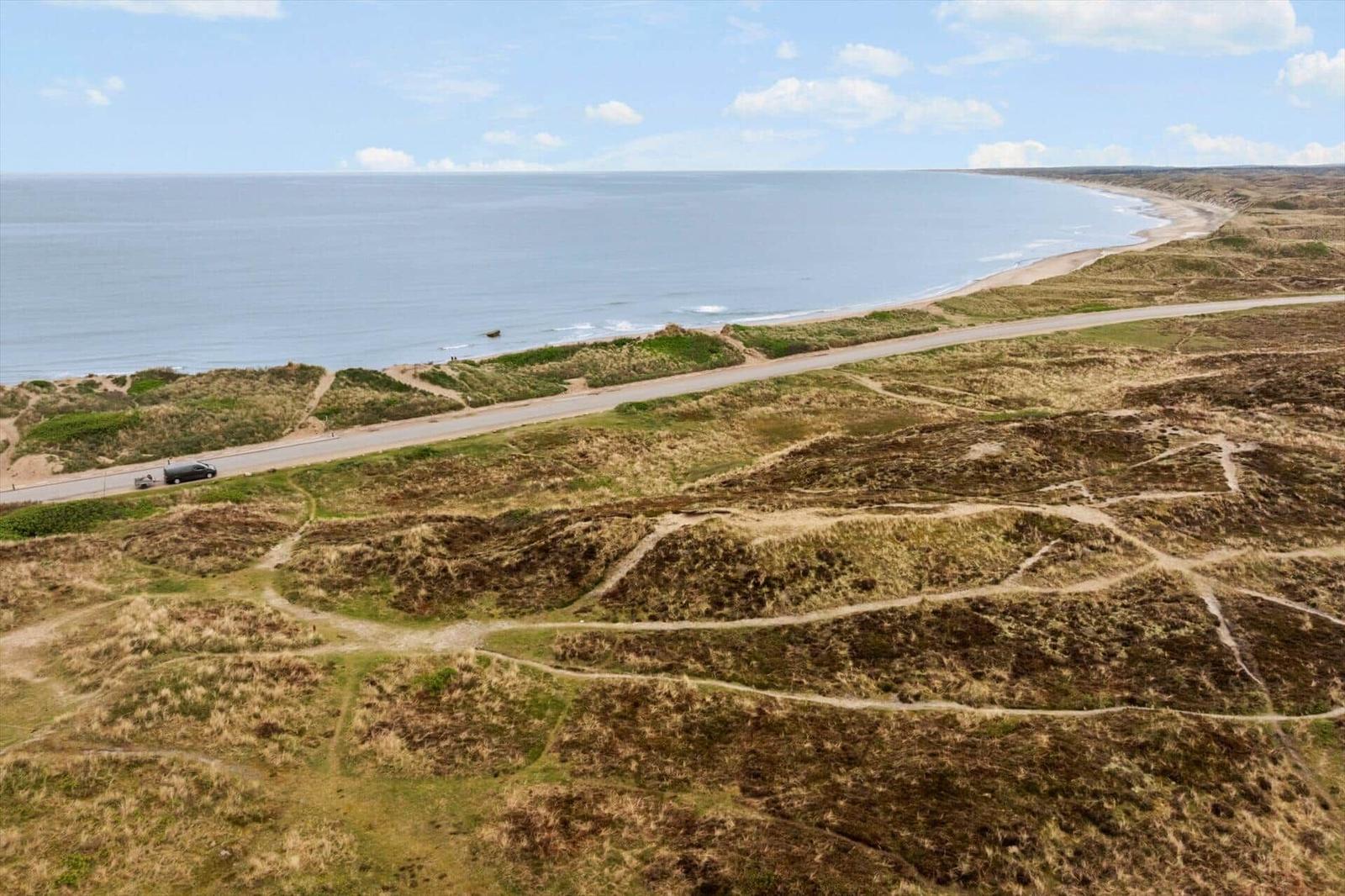 Meerstrand mit Dünen, Straße und einem Fahrzeug. Blick von oben auf Küstenlandschaft.