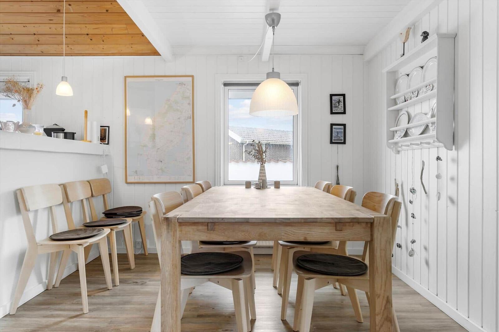 Esszimmer mit Holztisch, Stühlen und Fensterblick. Weiße Wände, Holzdecke und Küchenzeile.