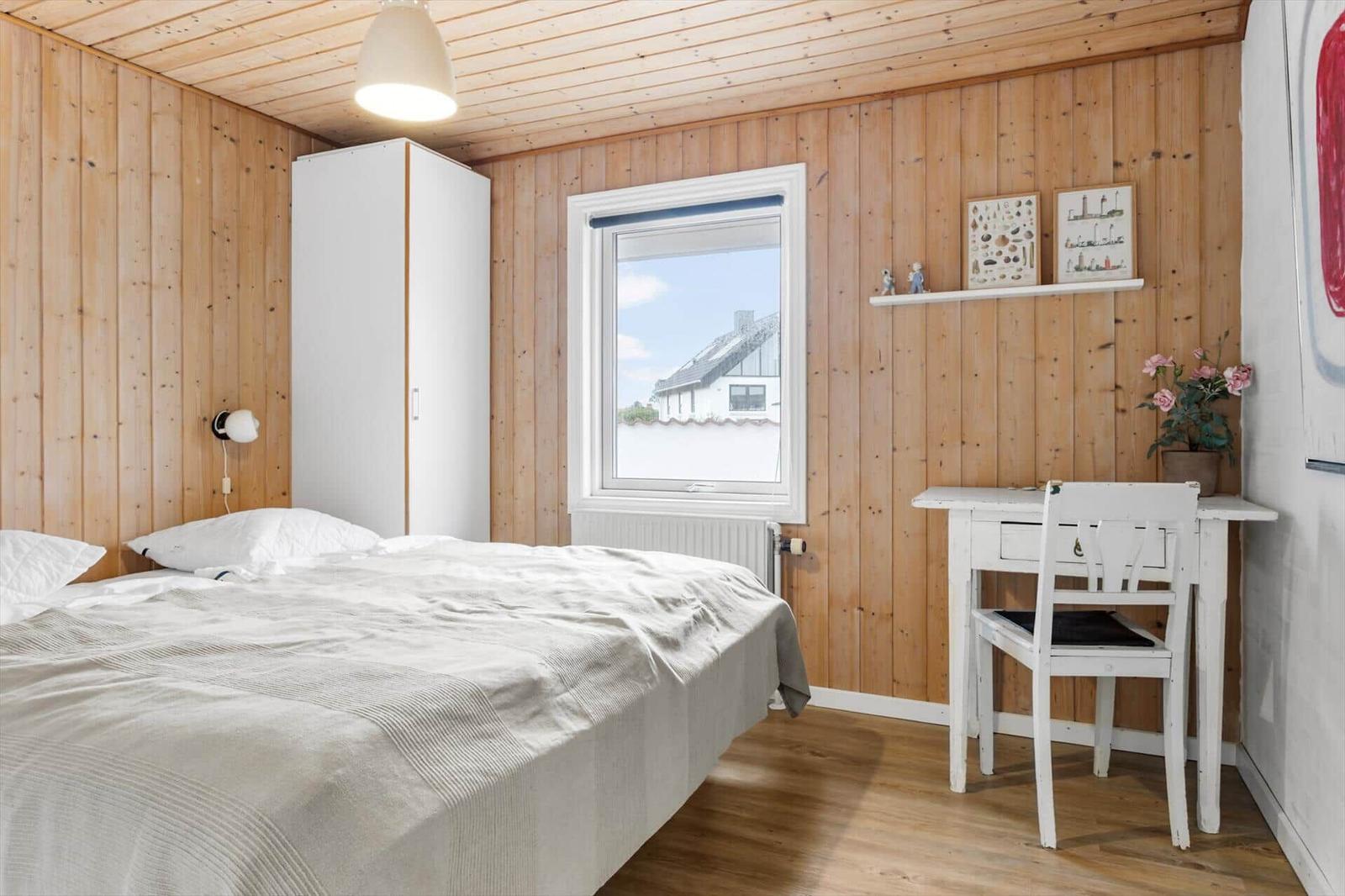 Schlafzimmer mit Holzwand, Bett, Schreibtisch und Fenster.