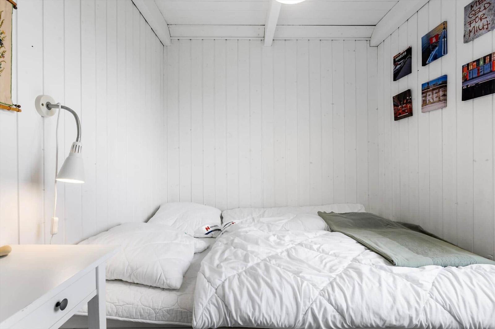 Schlafzimmer mit weißer Wandverkleidung, Bett mit weißen Kissen und Decke, Wandlampen und Bildern.