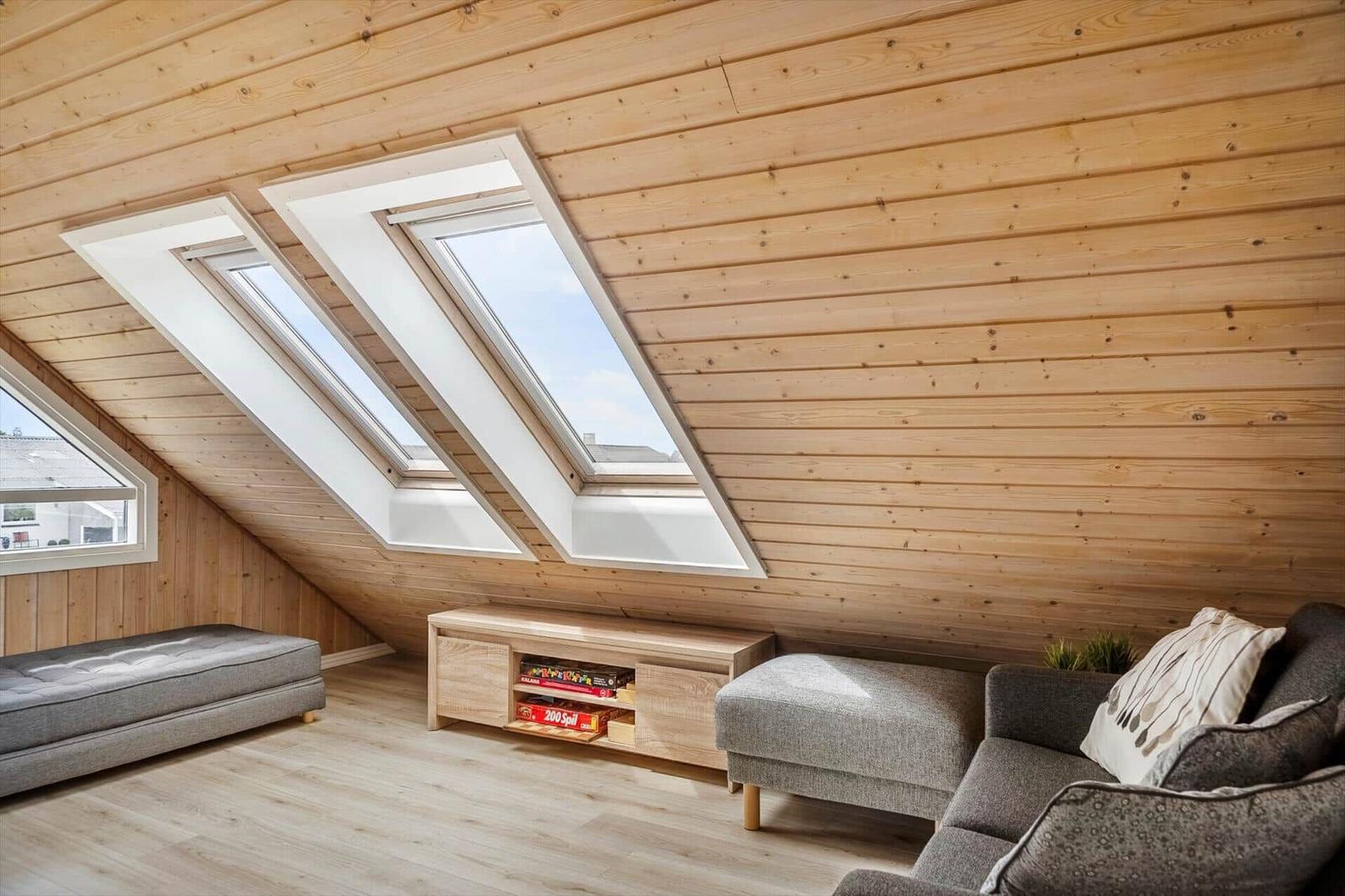 Wohnraum mit Holzwand, Dachfenstern und grauer Sofa-Ecke.