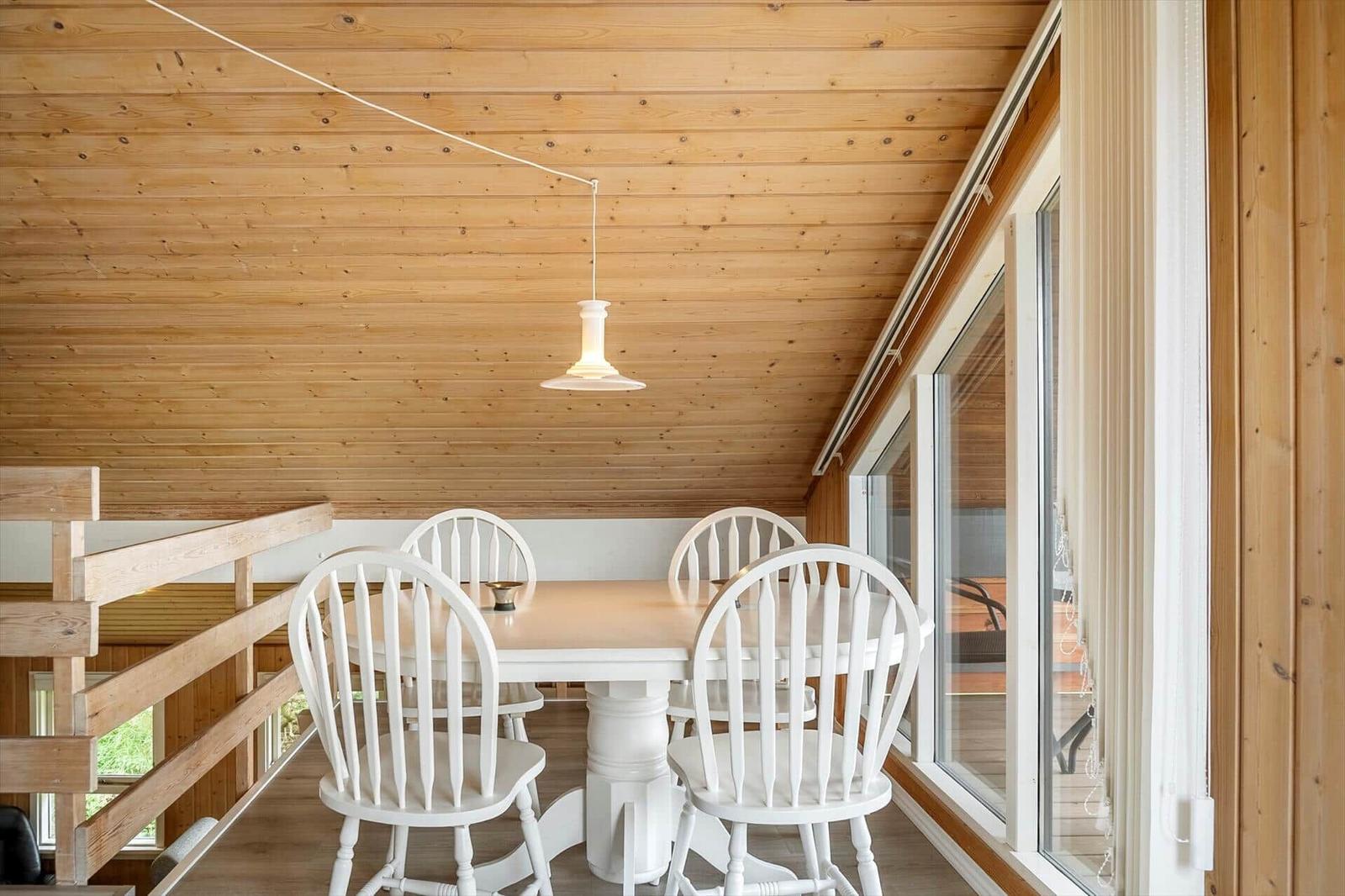 Essbereich mit weißem Tisch und Stühlen unter Holzdecke mit hängender Lampe.