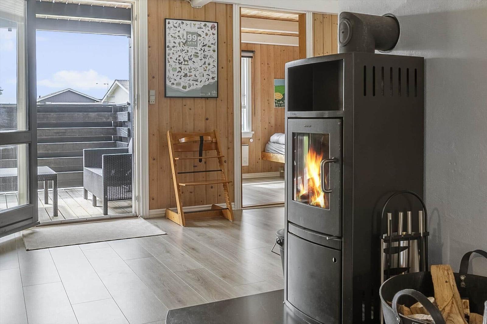 Kaminofen mit brennendem Holz, Terrasse mit Sitzgelegenheiten und Holzwand im Hintergrund.