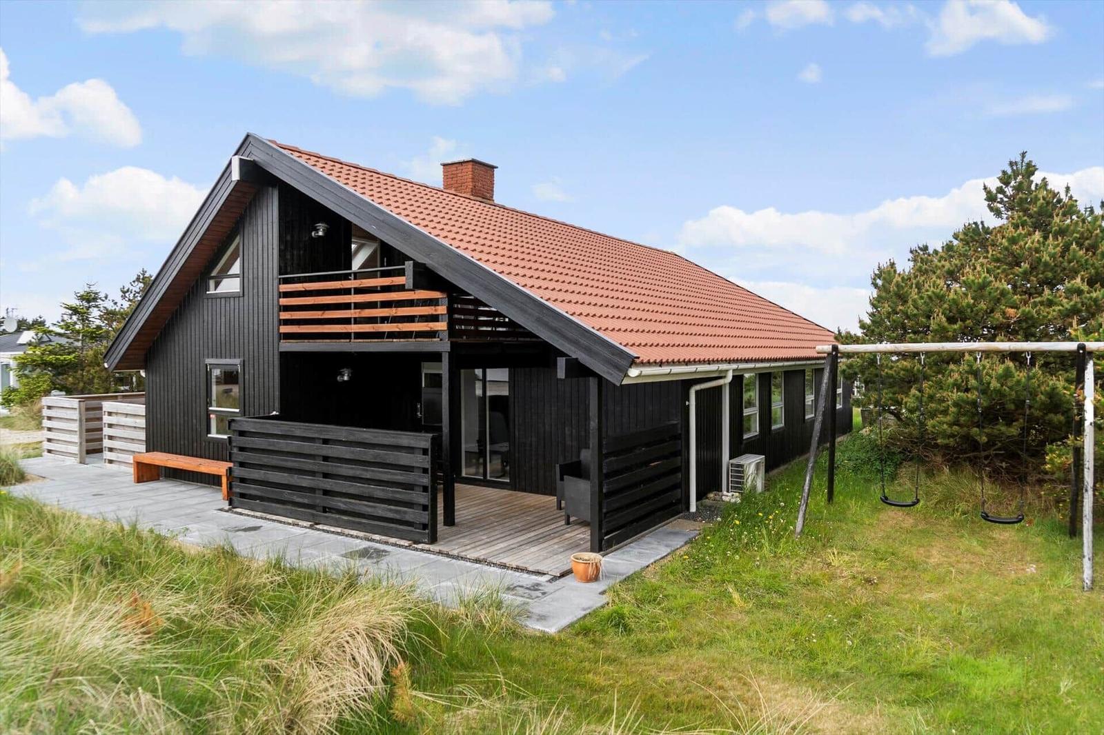 Ein schwarz gestrichenes Haus mit rotem Dach, Terrasse und Schaukel im Garten.