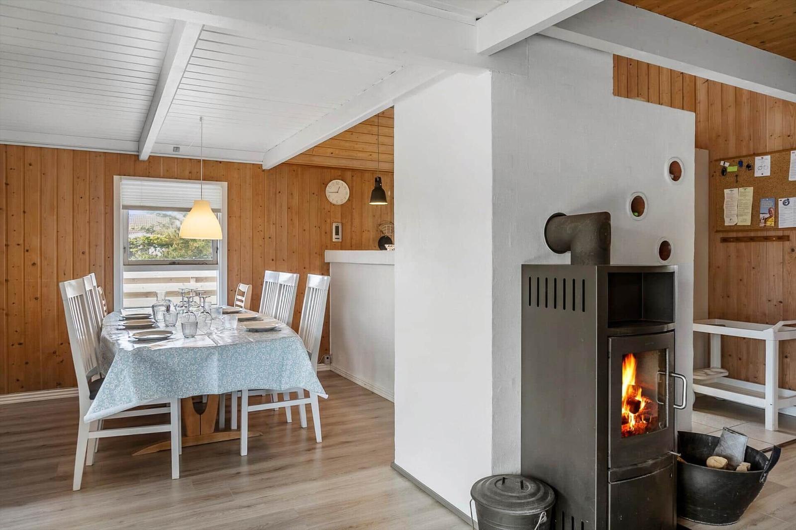 Essbereich mit Tisch und Stühlen, Kaminofen und Holzwand.