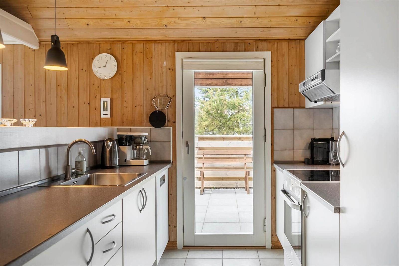 Küche mit Blick auf Balkon, weiße Schränke und Holzwand.