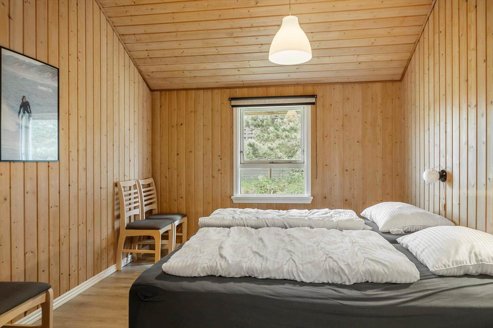 Schlafzimmer mit Holzwand, Bett, Fenster und Stühlen.