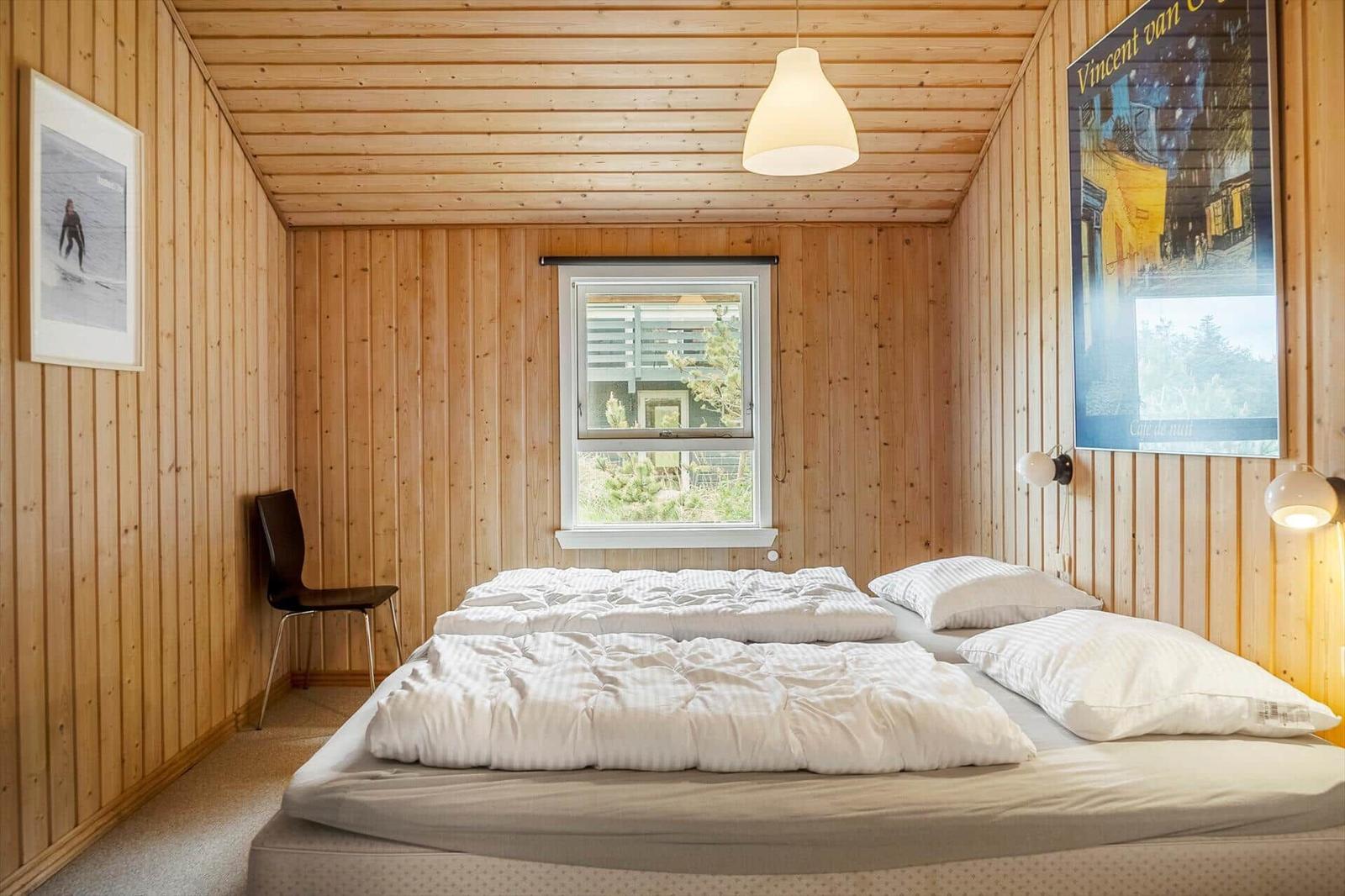 Schlafzimmer mit Holzwand, Bett, Fenster und Deckenleuchte.