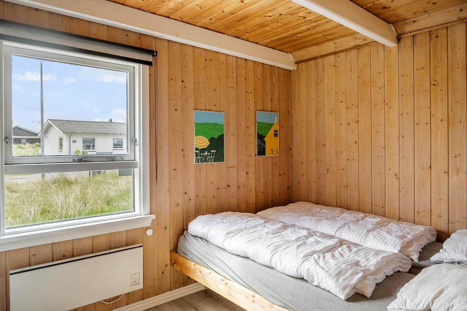 Schlafzimmer mit Holzwand, Bett und Fensterblick auf Grasland.