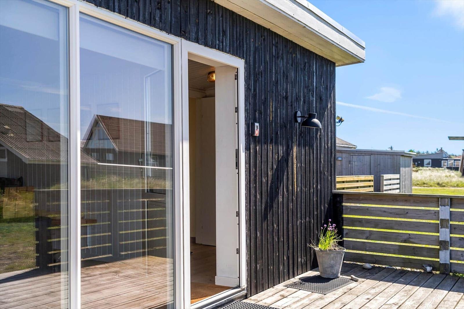 Schwarze Holzwand mit Glasfront und Terrasse. Pflanze im Topf neben der Tür.