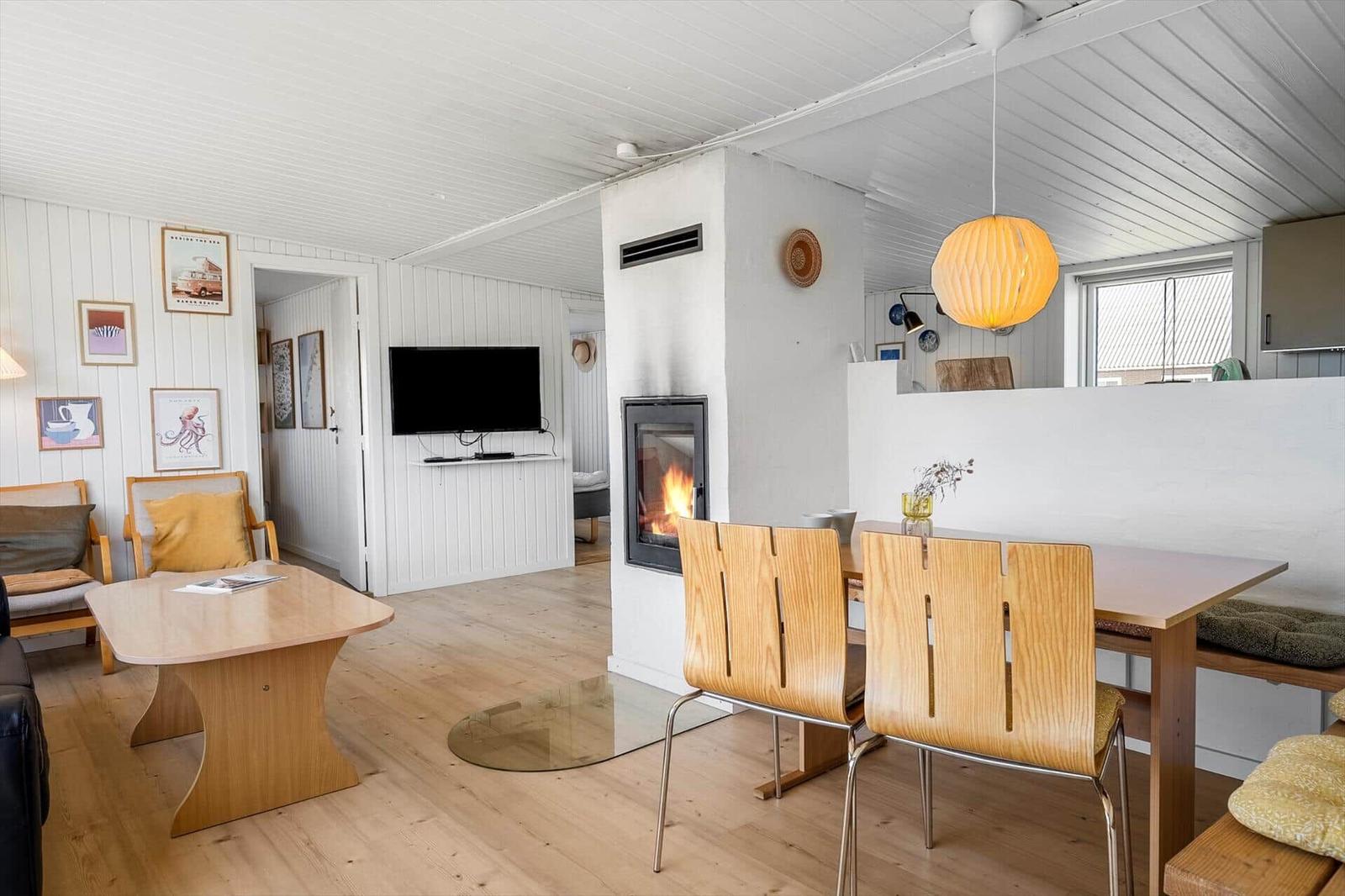 Wohnzimmer mit Esstisch, Kamin und Fernseher. Holzfußboden und weiße Wände.
