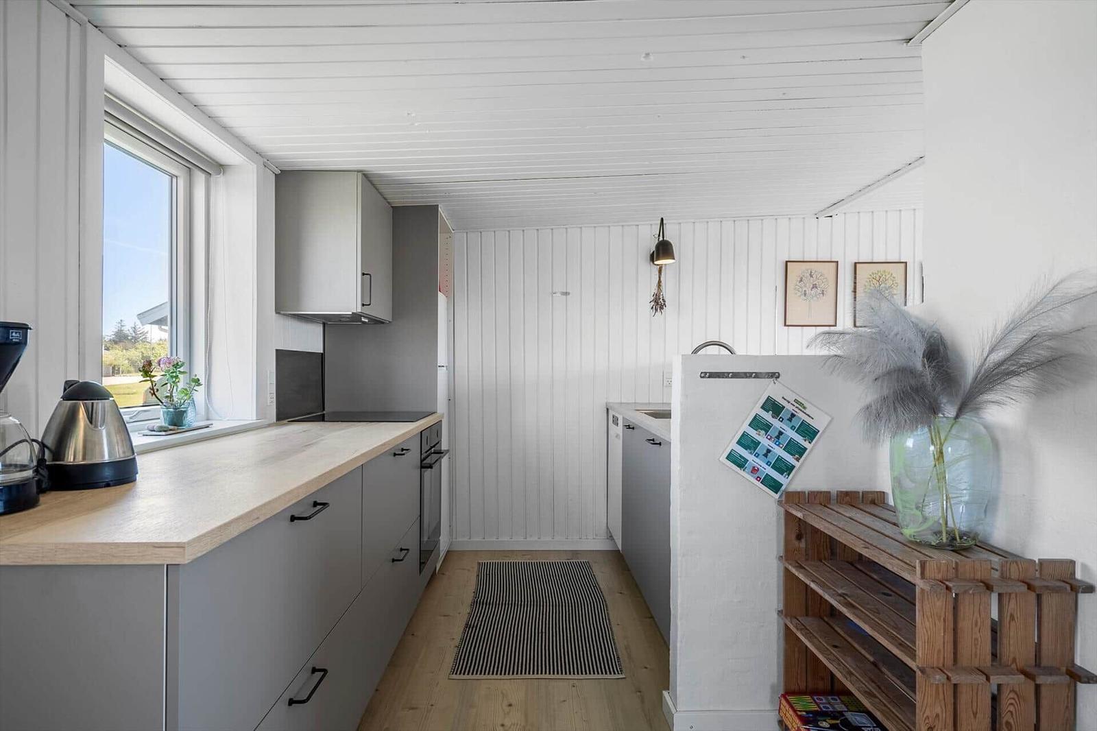 Küche mit grauen Schränken, Holzoberfläche und Fenster. Holzfußboden und weiße Wände.