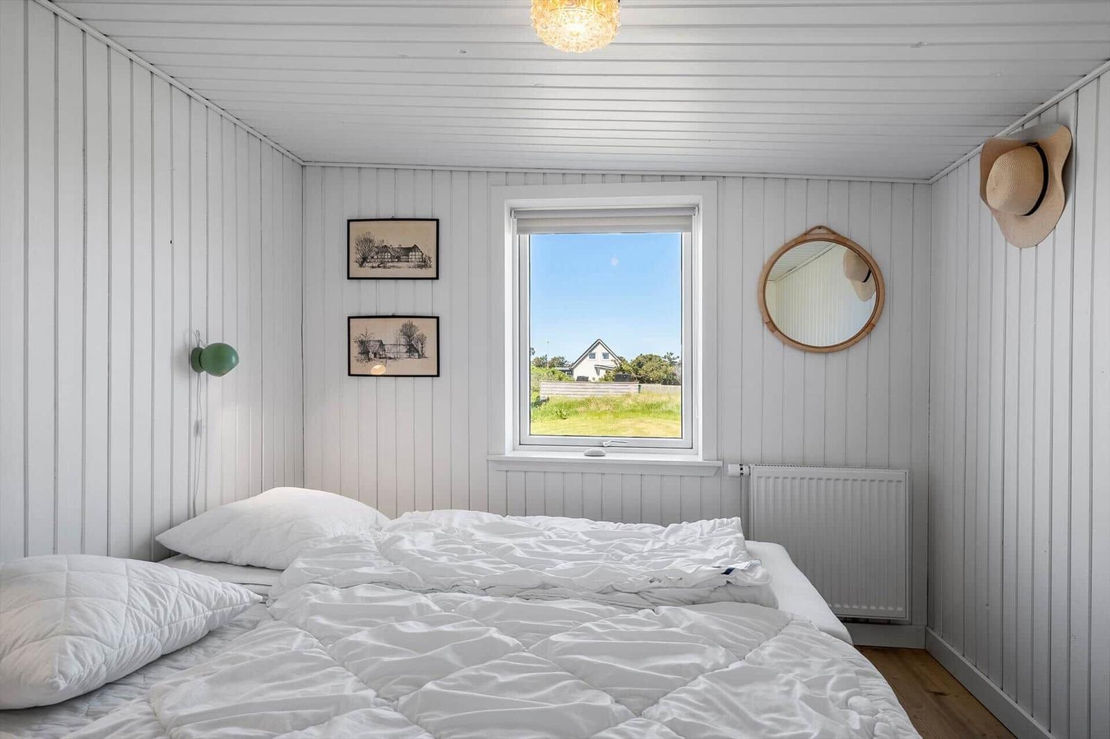 Schlafzimmer mit weißem Bett, Fensterblick und Wandbildern.