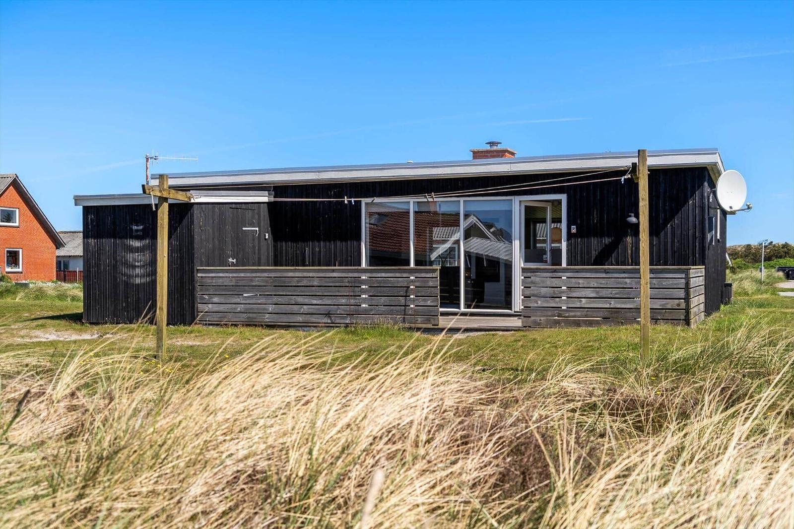 Moderne Holzhütte mit Balkon und Satellitenschüssel in Grasland.