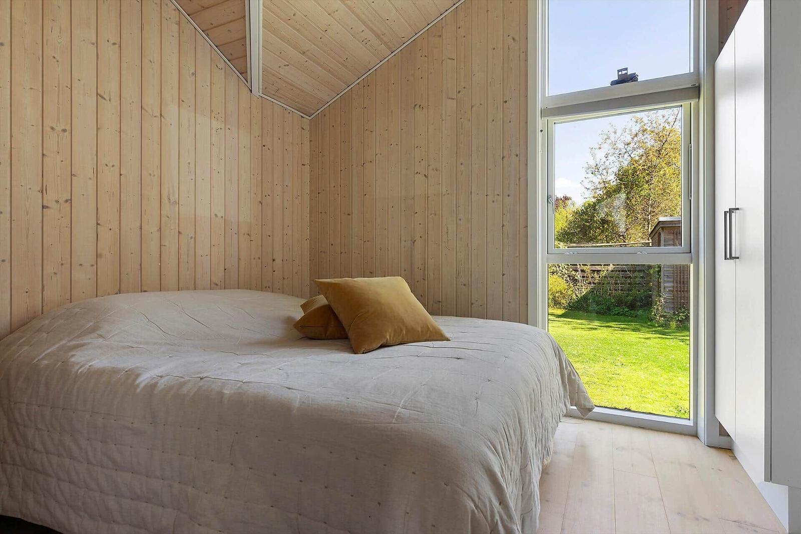 Bedroom with wooden walls and large window to the garden