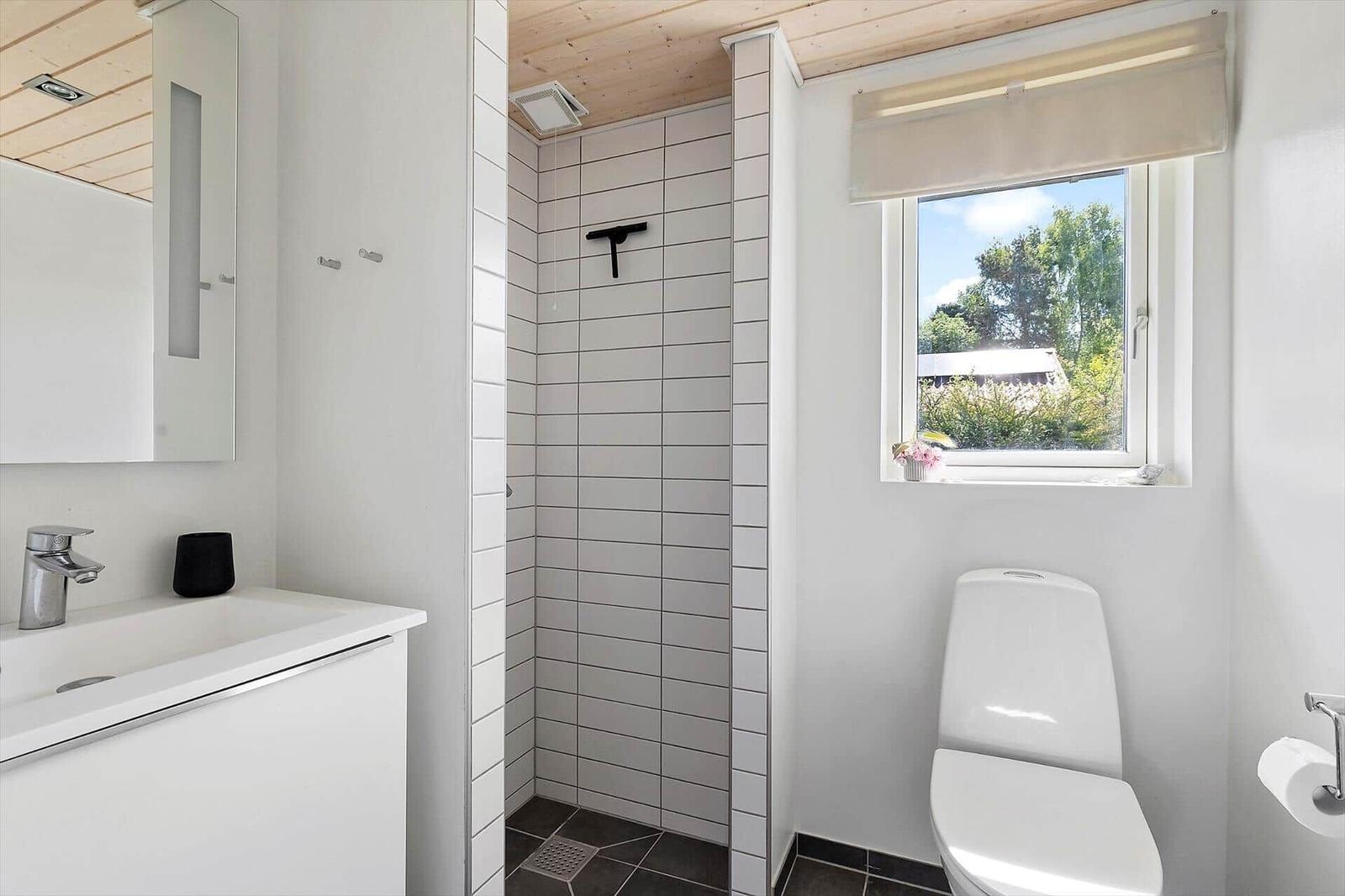 Bathroom with shower, toilet, and sink. Window with view of greenery.