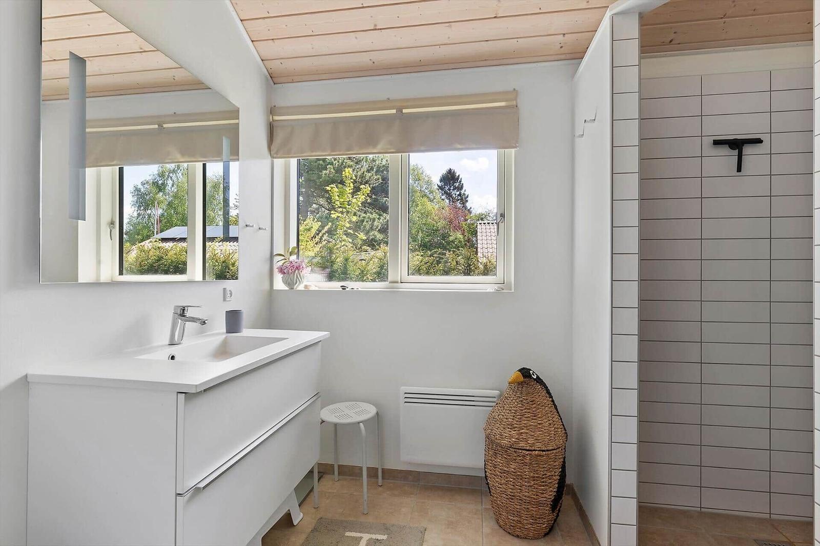 Bathroom with sink, shower, and window overlooking greenery.