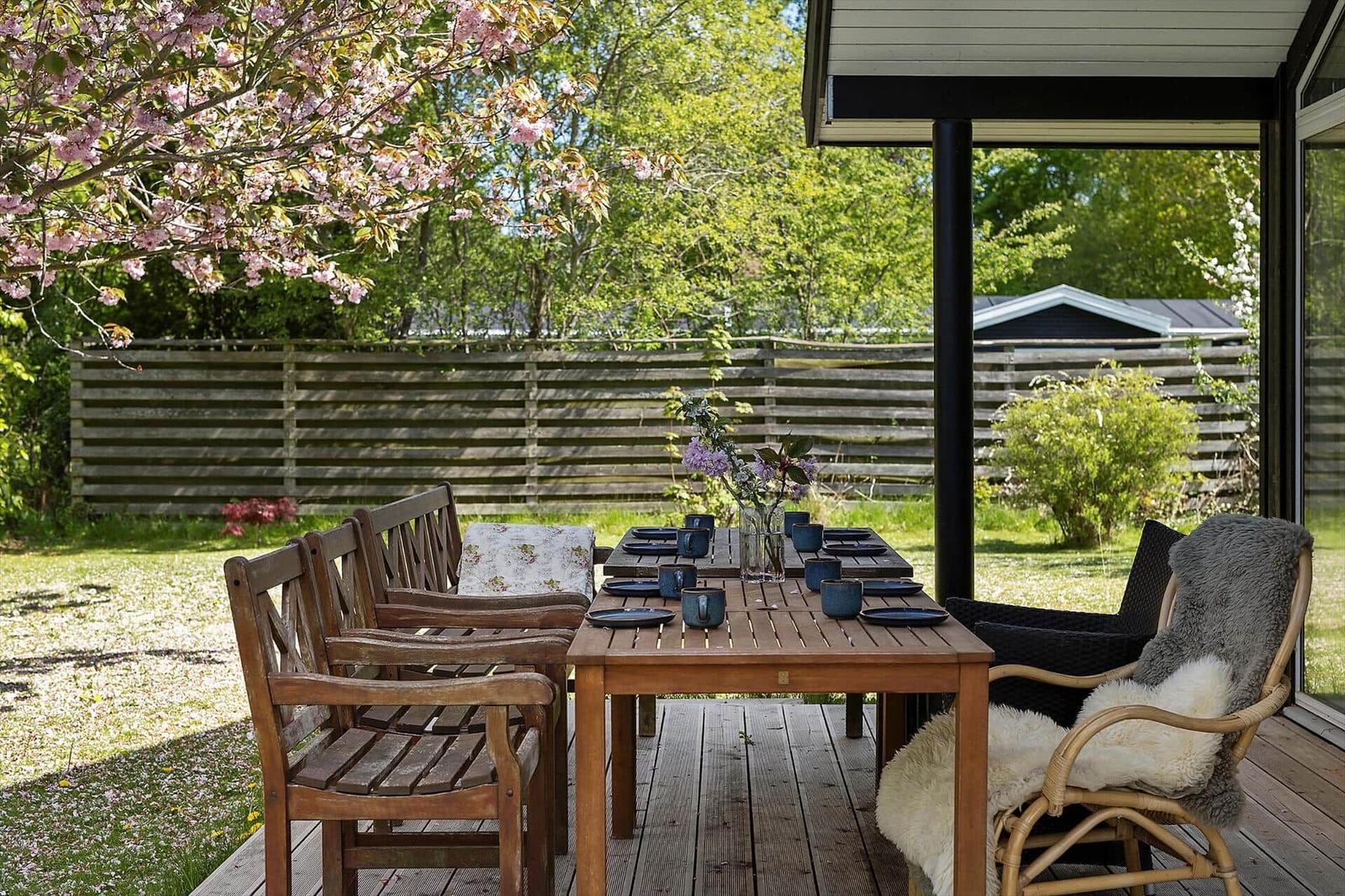 Patio with wooden table, chairs, and floral decoration under blooming trees.