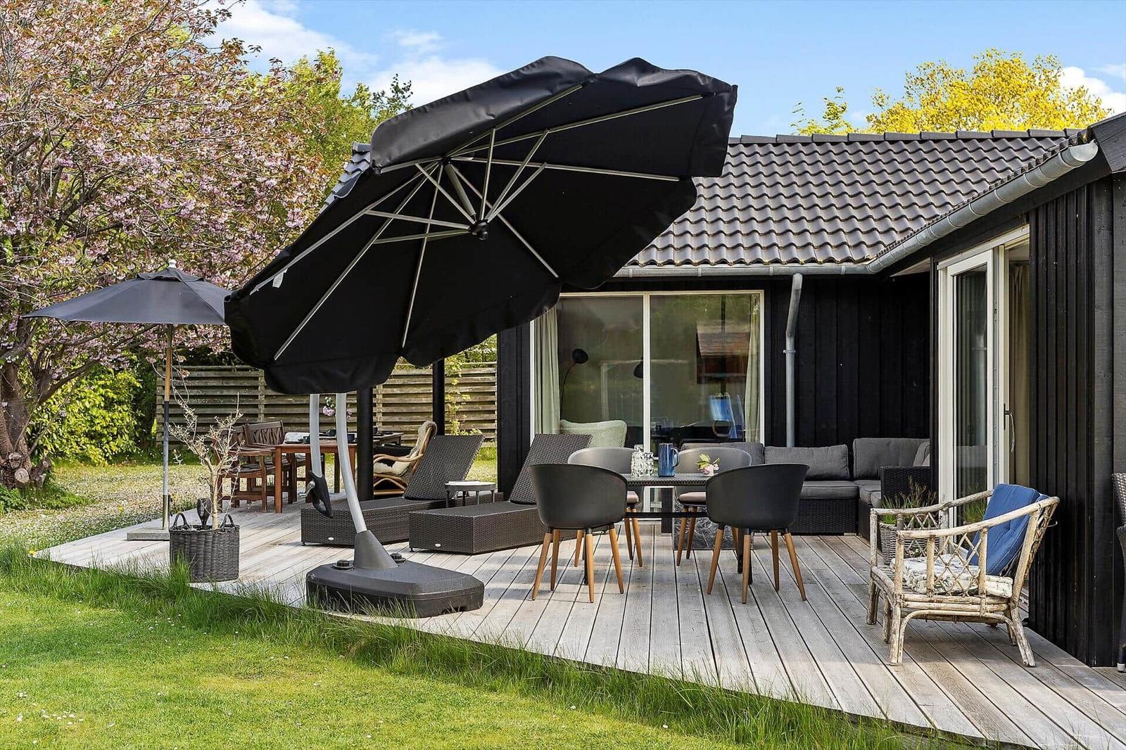 Deck with seating, umbrella, and garden. House with glass front and wooden cladding.