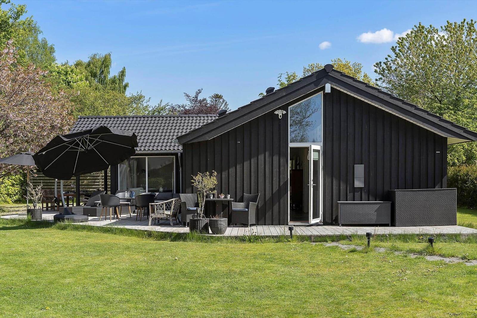 Black wooden house with terrace, garden, and seating under umbrellas.