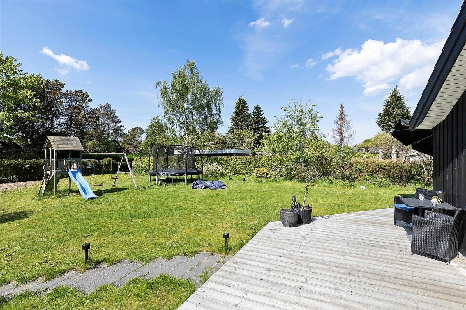 Backyard with playground, trampoline, and wooden terrace with seating area.