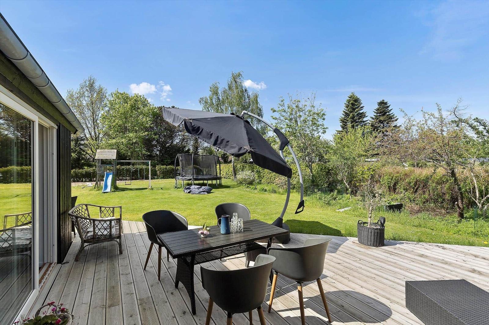Deck with table, chairs, and umbrella. Lawn and play equipment in background.