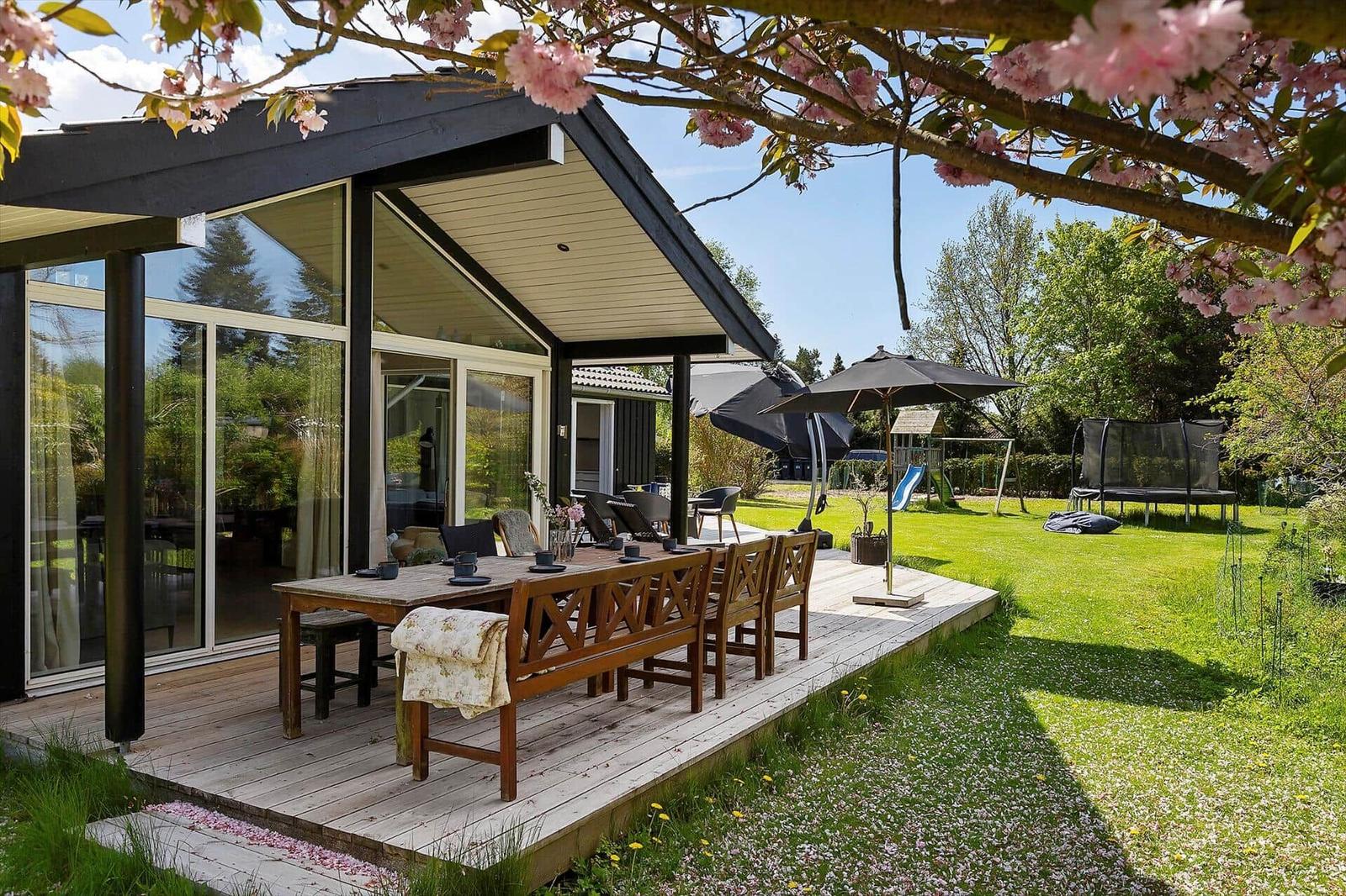 House with terrace, garden, and dining area under blooming cherry trees.