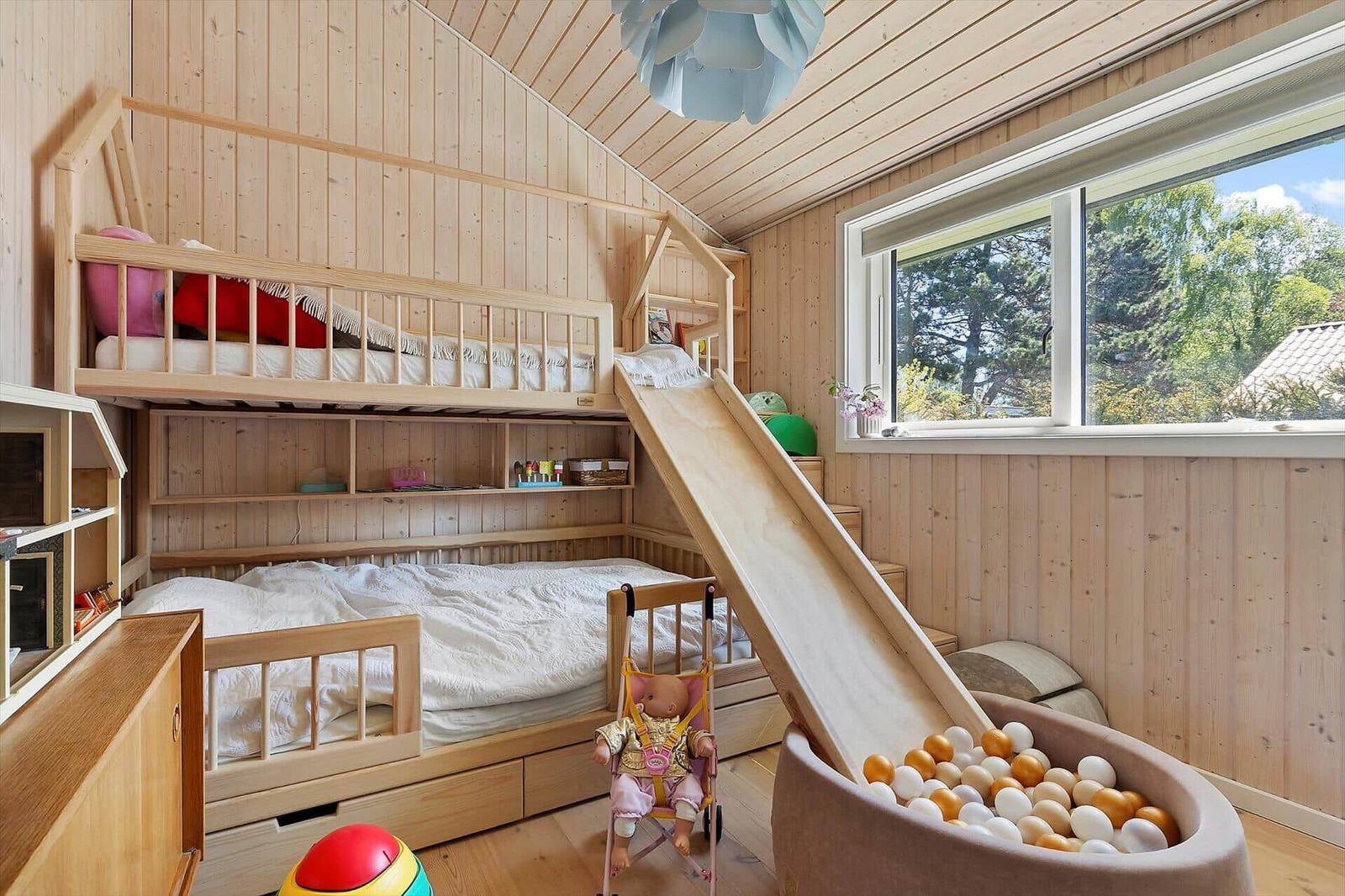 Childrens room with loft bed, slide, and ball pit. Wooden walls and large window.