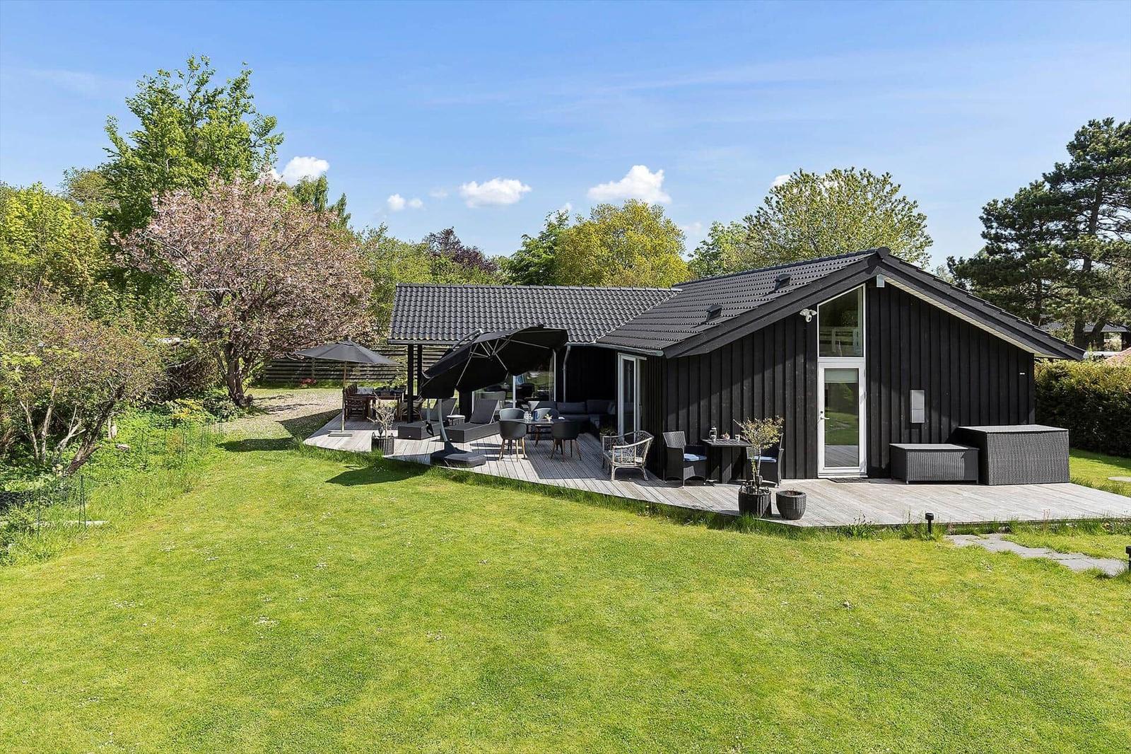 Black house with terrace, garden, and seating under umbrellas.