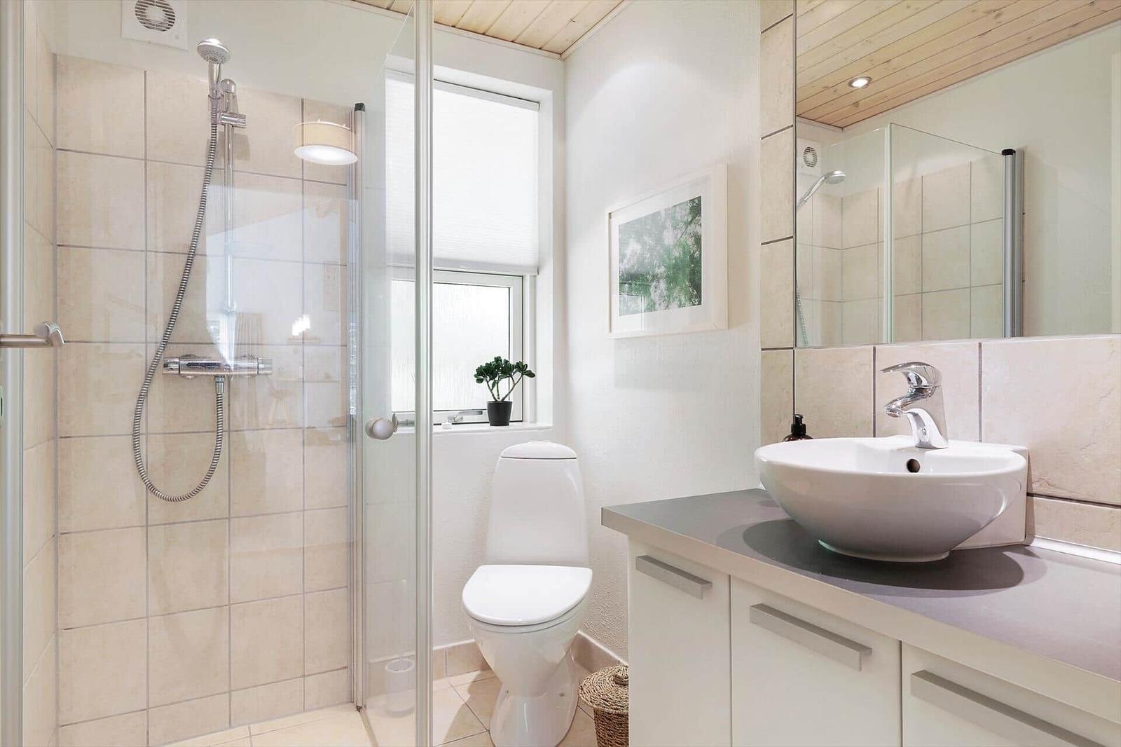 Bathroom with shower, toilet, and sink. Window with plant.