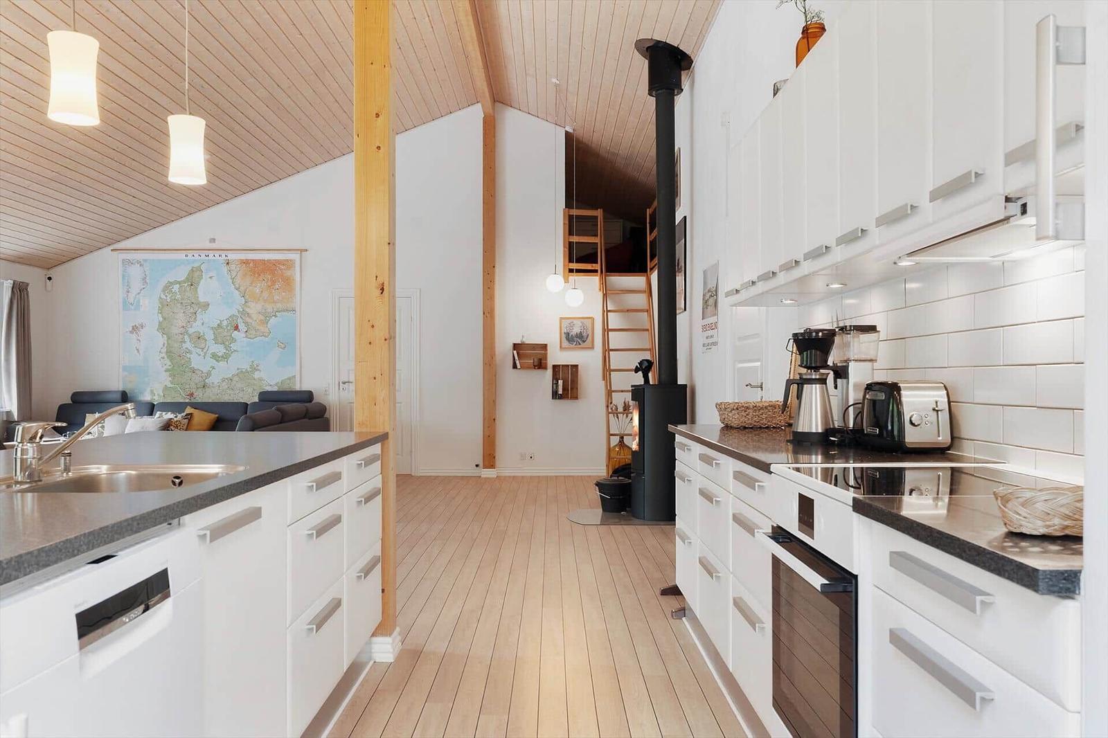 Kitchen with white cabinets and wooden floor. Living room with sofa and map in background.