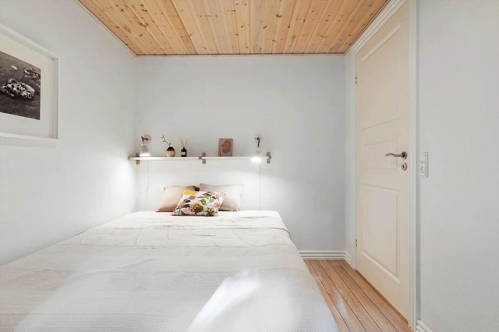 Bedroom with bed, wooden ceiling, and wall shelf with lamps.