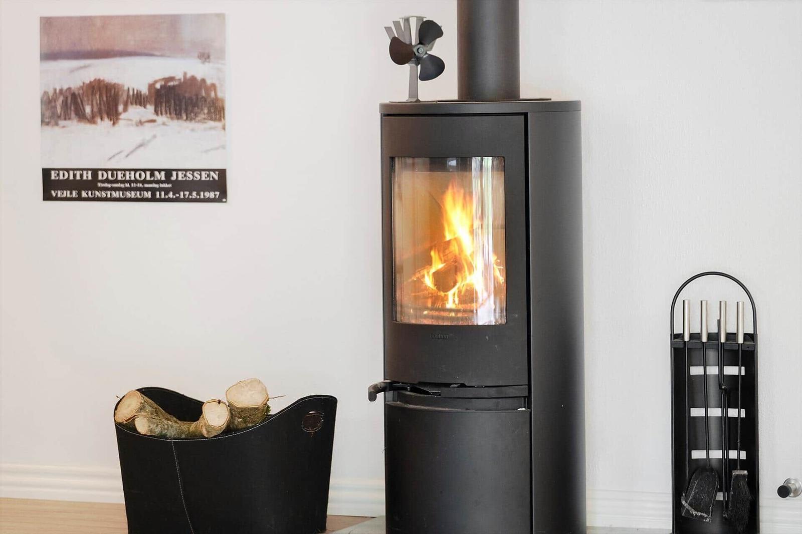 Black wood-burning stove with burning logs, fire tools on wall beside it.