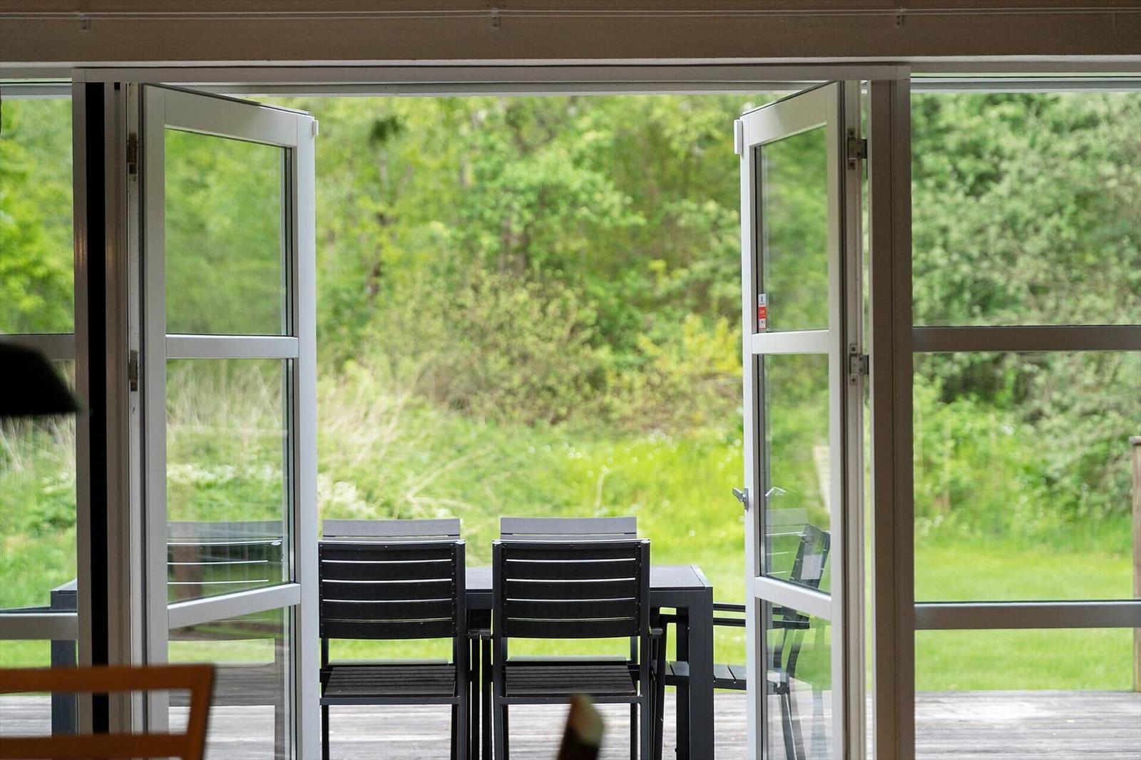 Sliding glass doors open to a terrace with table and chairs. Green garden in the background.