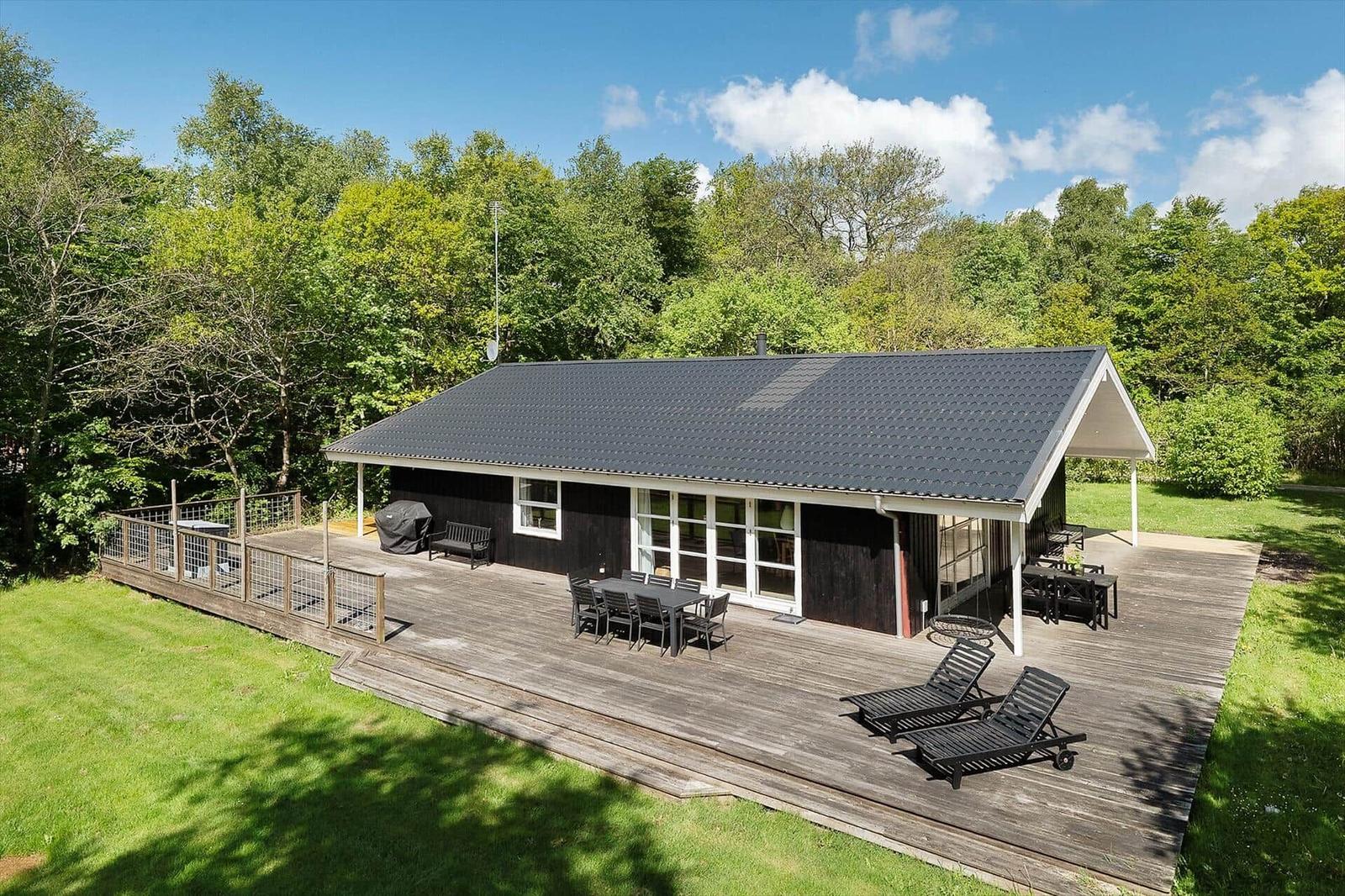 Modern wooden cabin with large deck, garden furniture, and view into the forest.