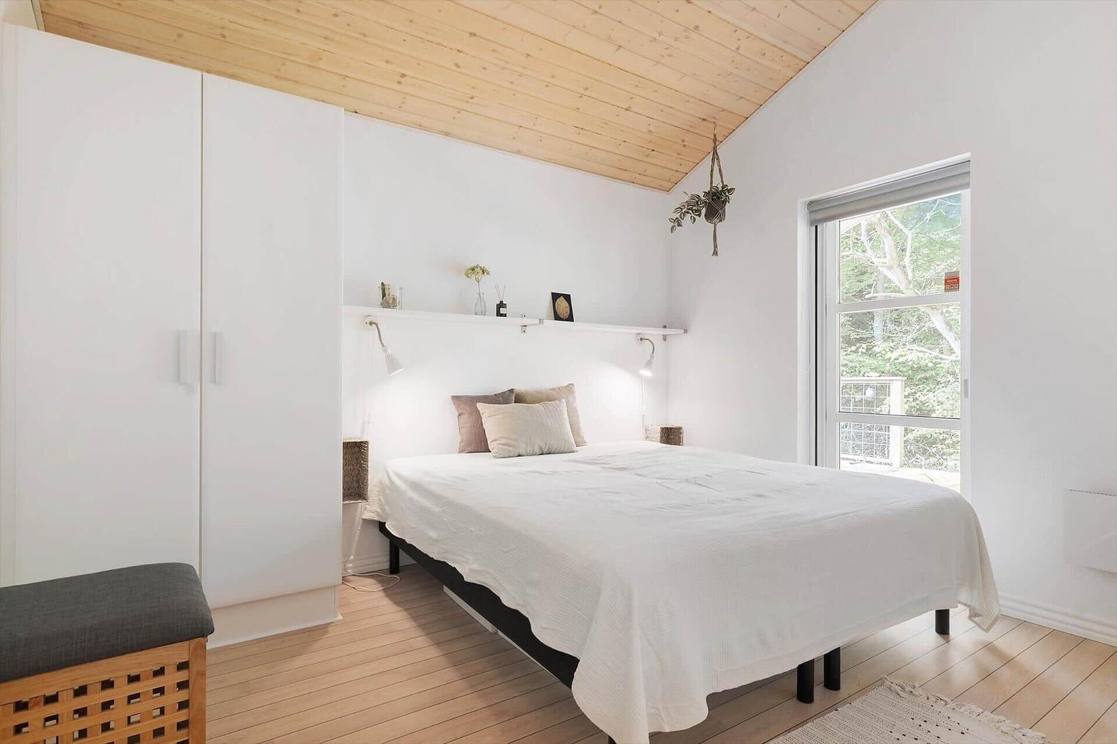 Bedroom with white bed, wooden ceiling, and window to the garden