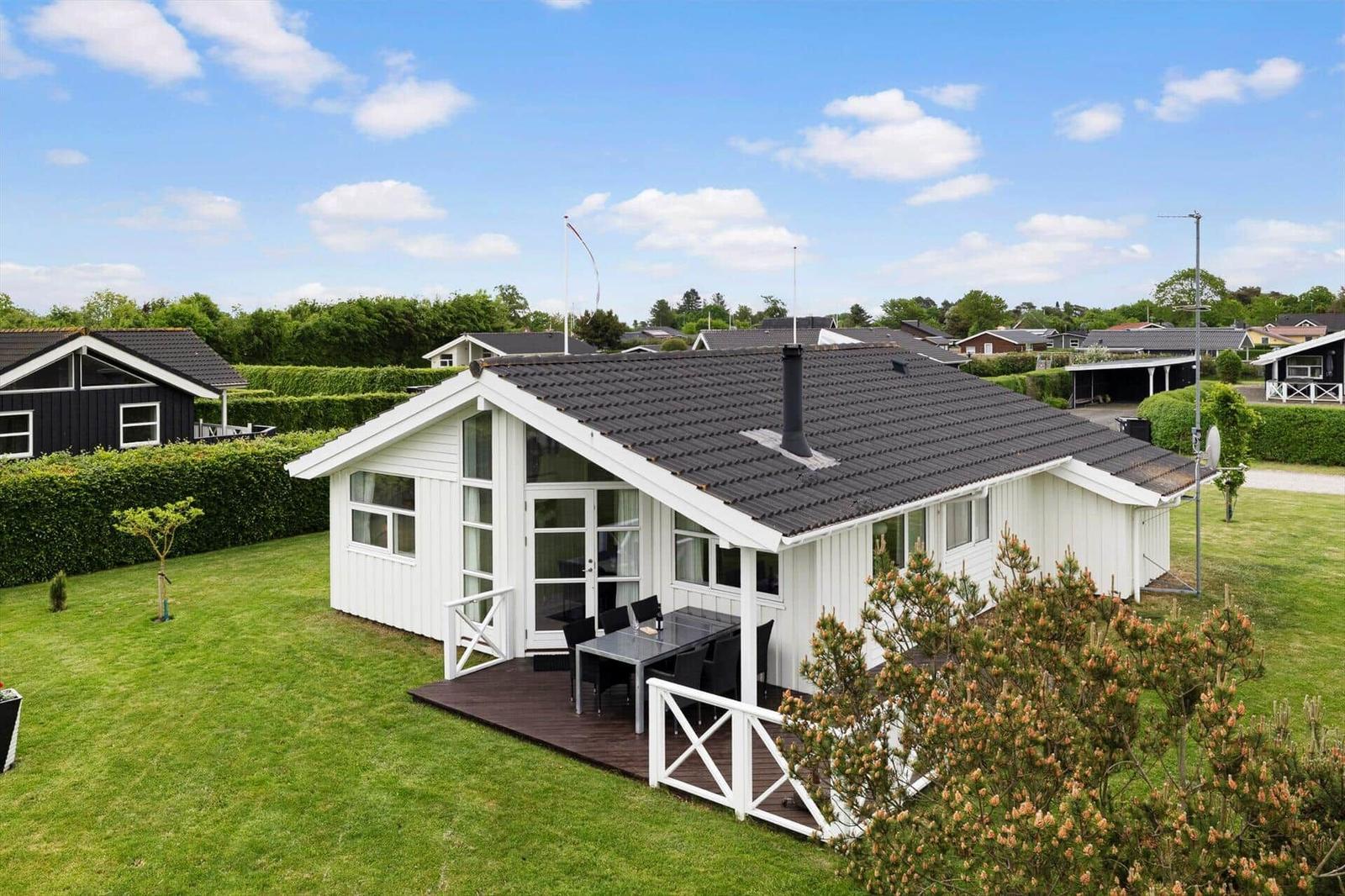 Weißes Ferienhaus mit Terrasse und Garten unter blauem Himmel.