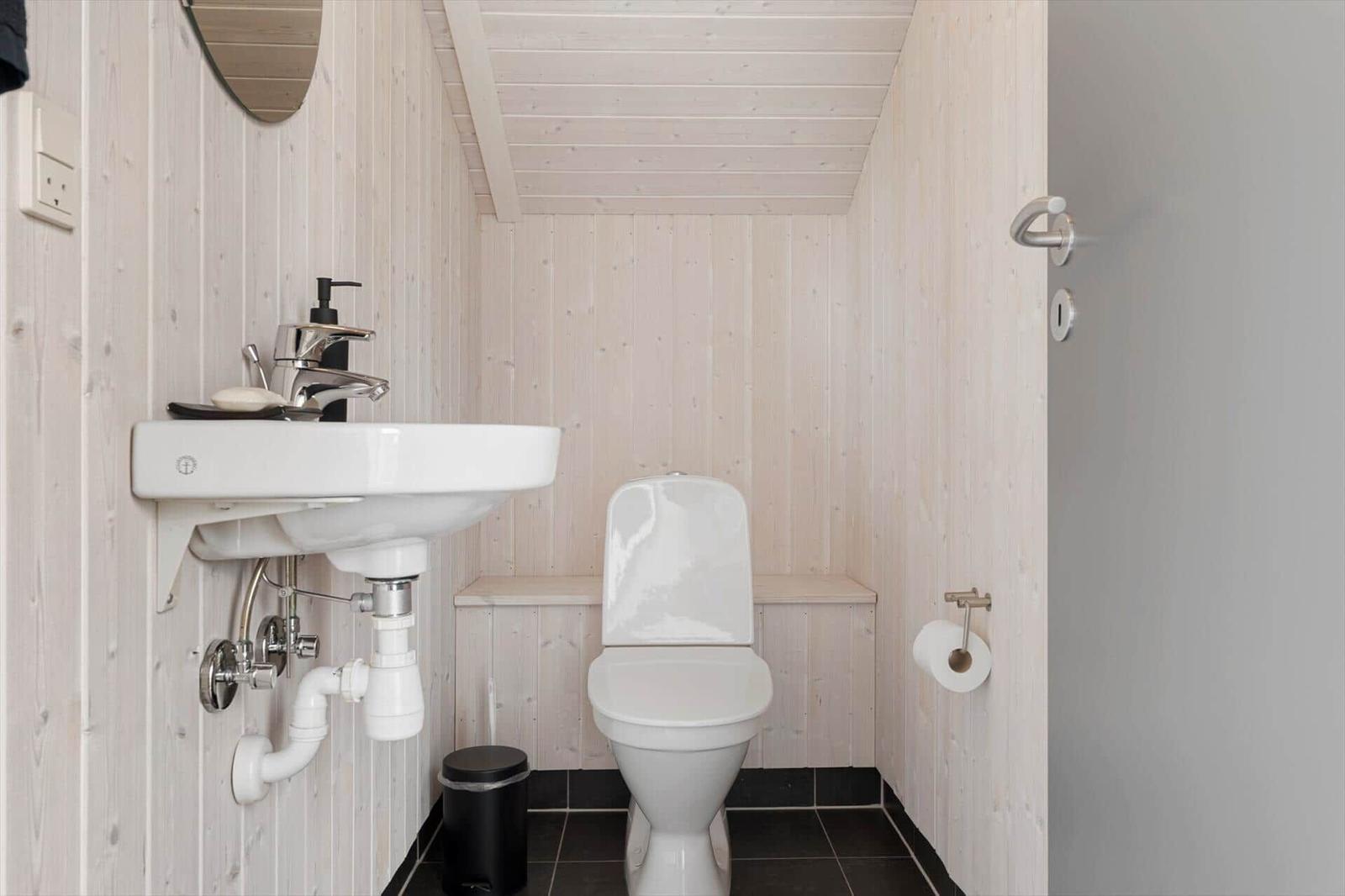 Badezimmer mit Toilette, Waschbecken und Spiegel an Holzwand.