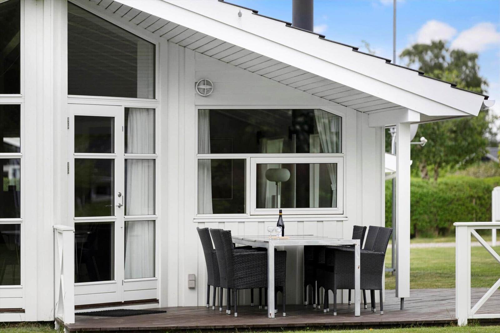 Wohnung mit Terrasse, Tisch und Stühlen. Weiße Fassade und Holzdecke.