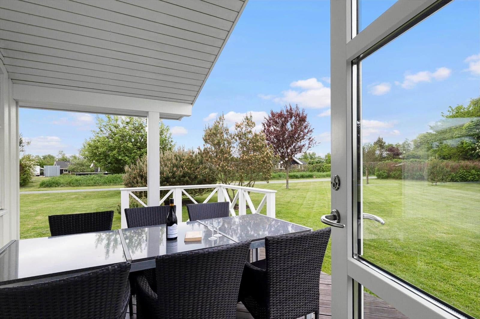 Terrasse mit Tisch und Stühlen, Blick auf grünen Rasen und Bäume.