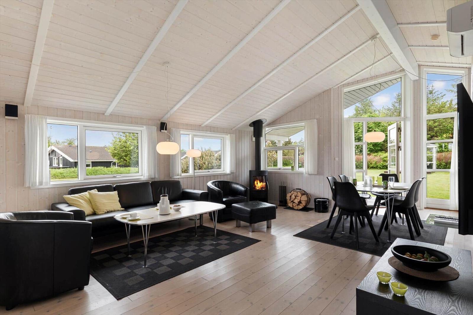 Wohn- und Essbereich mit Kamin, schwarzer Ledermöbel und Holzboden. Große Fenster mit Blick auf Garten.