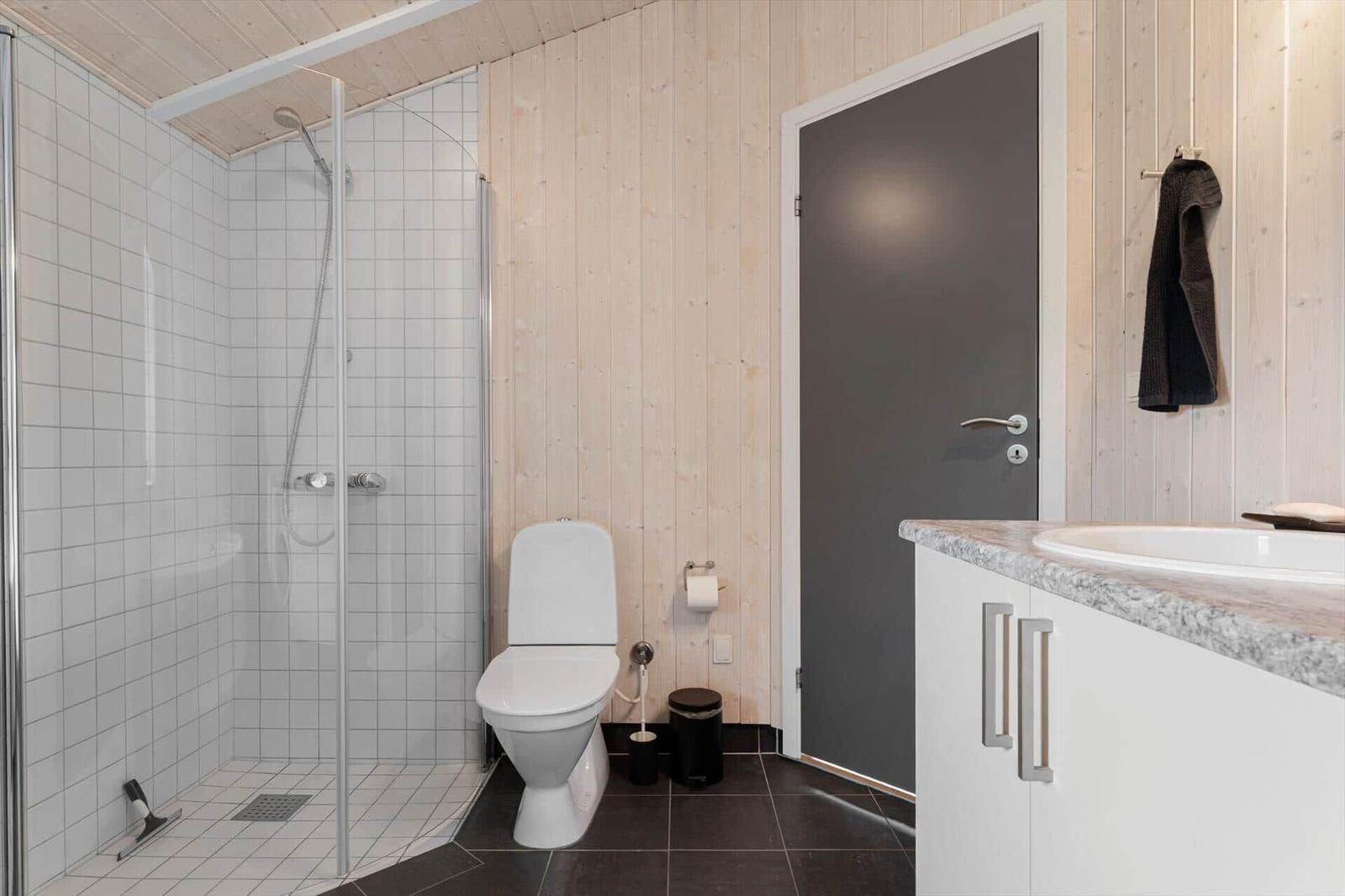 Badezimmer mit Dusche, Toilette und Waschtisch. Holzwände und dunkler Boden.