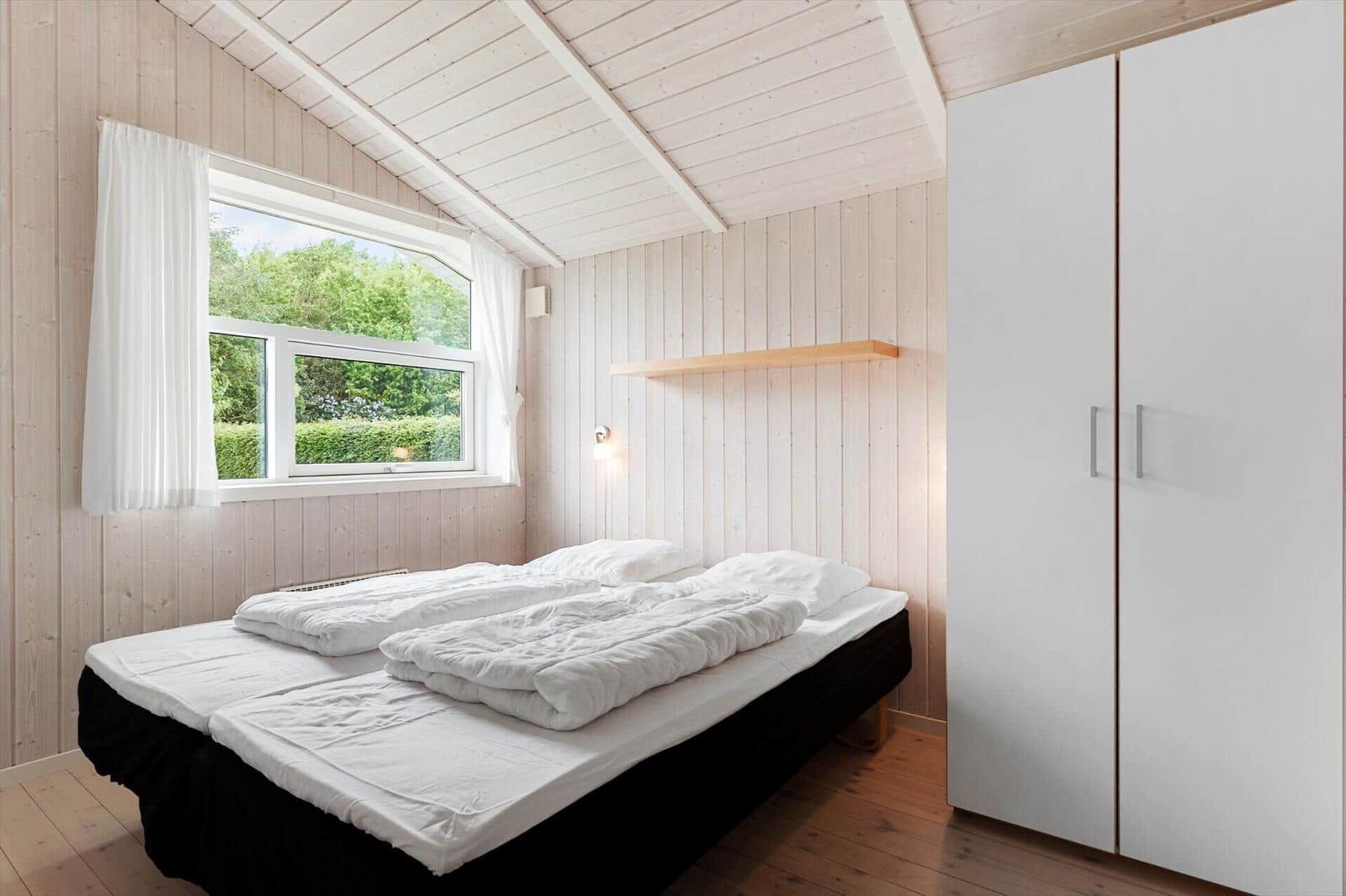 Schlafzimmer mit Doppelbett, Fenster und Kleiderschrank. Holzwände und -decke.