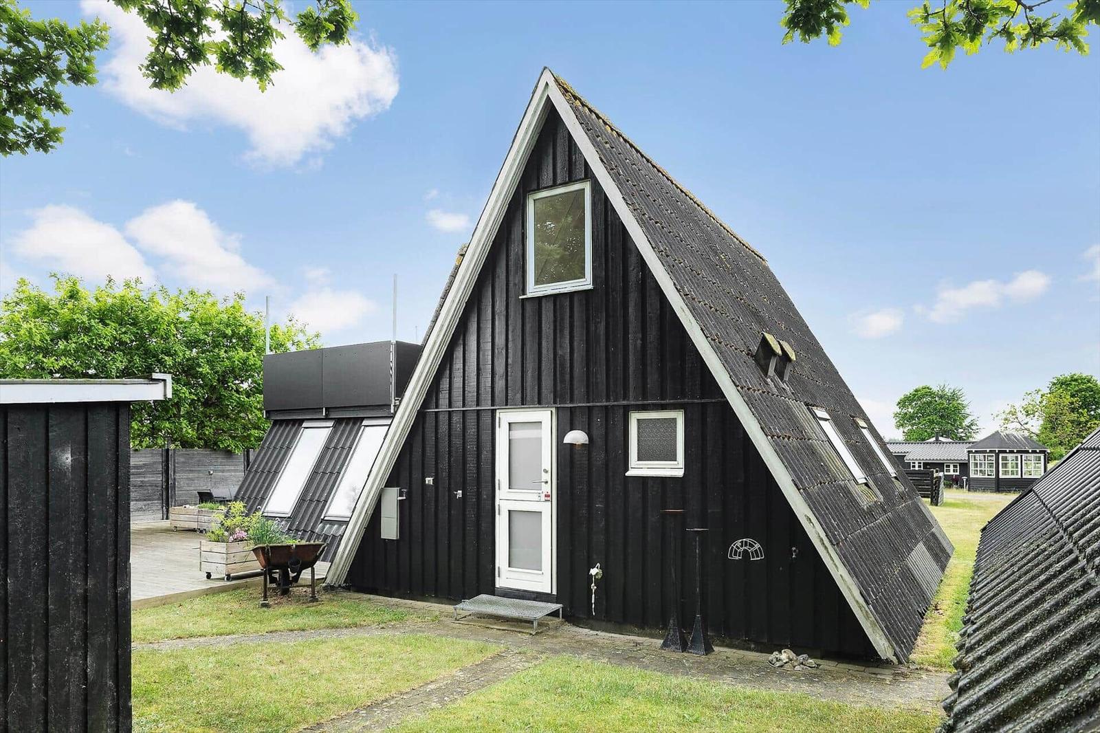 Schwarzes A-Fassadenhaus mit weißen Fenstern und Tür. Gartenbereich mit Pflanzen.