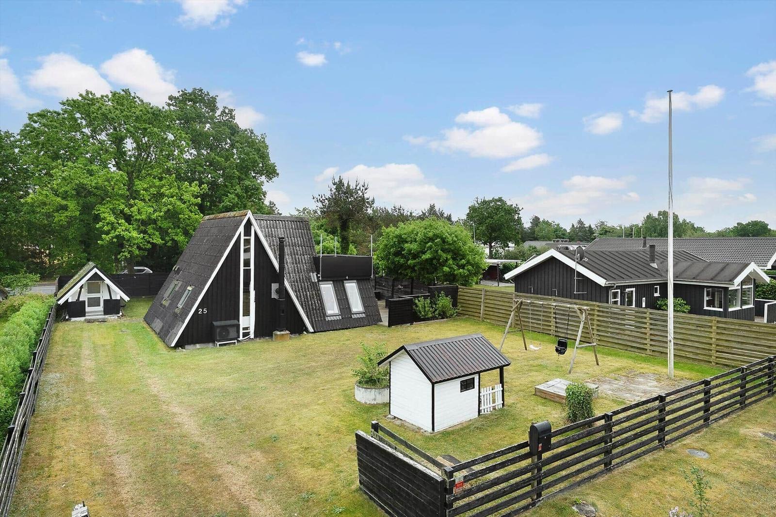 Schwarze Holzhäuser mit Garten und Spielplatz unter blauem Himmel.
