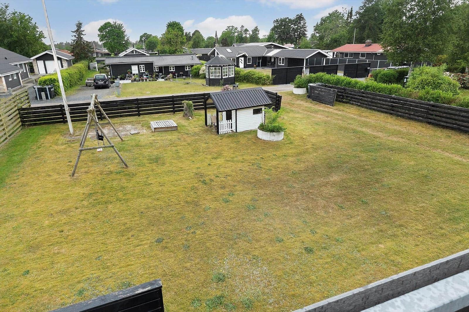 Großer Garten mit Schaukel, kleinem Holzhaus und umzäuntem Grundstück.