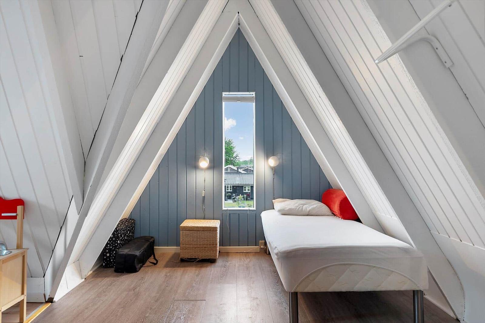 Ein Schlafzimmer mit Dachschrägen, Bett, Fenster und Korb.